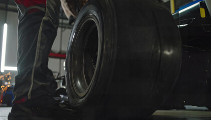 Fototapeta premium Mechanic Standing Beside Racing Car Tire in Motorsport Pit Garage