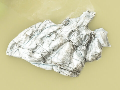 Aerial view of a solitary iceberg, etched with dark lines, drifts in the glacial lagoon's milky waters, a stark monument to the receding ice, Solheimajokull, Myrdalshreppur, Iceland.