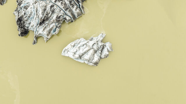 Aerial view of glacial icebergs float serenely in the milky waters of the lagoon, a stark contrast of icy blues and earthy yellows, Solheimajokull, Myrdalshreppur, Iceland.