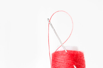 Sewing needle with red thread through the white background