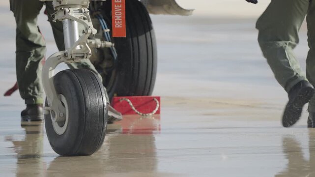 Close view of aircraft landing gear as ground crew removes a red wheel chock from the tire on a wet runway during departure preparation