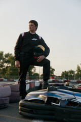 A confident go-kart racer strikes a powerful pose beside his kart on the track