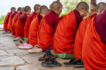 Sangchhen Dorji, Bhutan - 19 September 2025: View of maroon-robed nuns seated in silent meditation on stone, their varied footwear a colorful counterpoint to monastic uniformity.