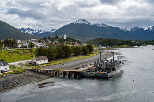 Aerial view of a small harbor town nestled between the calm waters and rugged, snow-capped Dientes de Navarino mountains, a scene of tranquil beauty, Puerto Williams, Chile.