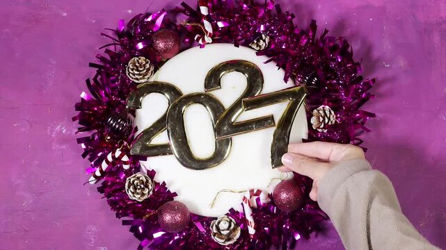 Golden 2027 numerals sit among Christmas and New Year decor&mdash;pinecones, candy canes, purple tinsel. Ideal for holiday campaigns, celebrations, and festive imagery