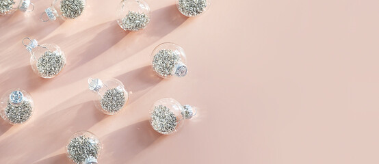 Glass Christmas ornaments scattered on light pink surface with copy space.
