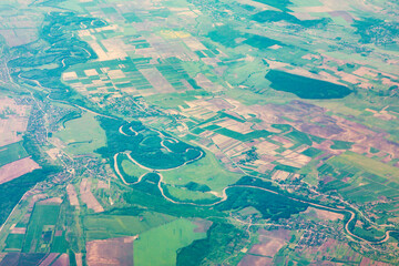 Winding river snakes through a mosaic of farmland and villages, its curves revealing a mature flow. Fields of varied hues and clustered homes reflect deep connection between water and rural life