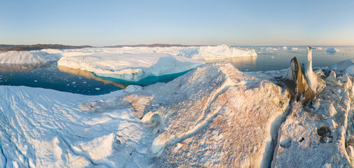 Panorama of large floating glaciers near Ilulissat Icefjord in western Greenland at sunset. Global warming and climate change. Most popular tourist destination. Summer time, aerial shot. Blue ocean 