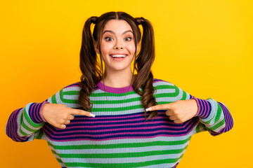 Young woman with colorful striped sweater smiles and points at herself against a bright yellow background product promotions