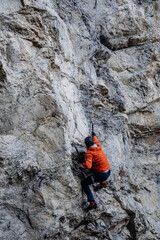 Male Dry Tooling Climber In Red Jacket On Steep Rock Face: Technical Ascent Using Ice Axes, Crampons, And Rope On Vertical Limestone Cliff