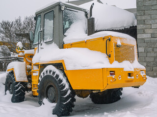A bulldozer for clearing roads of snow during a snowfall. A bulldozer with large wheels for road construction works stands in a snowdrift in winter. Road equipment.