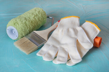 Gloves, a roller, and a brush on a green background. Tools for room renovation. Apartment renovation concept