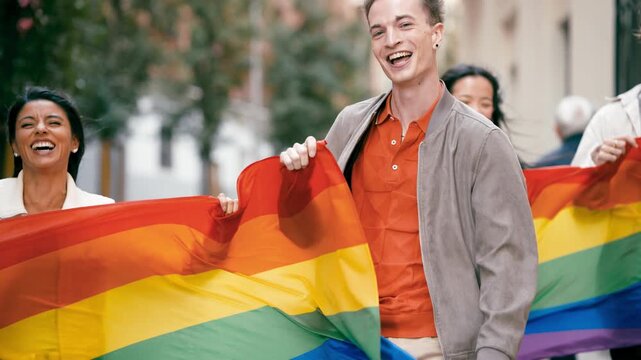 Group of happy multicultural friends smiling and walking down the street during a gay pride parade, holding a large rainbow flag together
