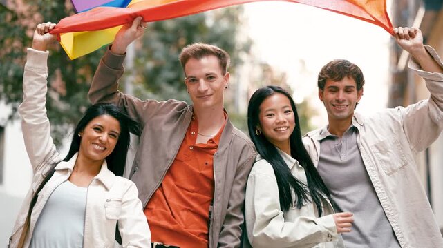 Multicultural group of young happy people supporting lgbtq rights. Cheerful friends smiling together while holding a large rainbow flag