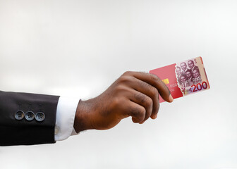 Dark-skinned hand in a black suit jacket holds a red, Ghana cedi banknote-themed credit card...