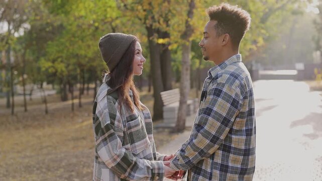 Side view young fun couple two friends family man woman wearing casual clothes together hold hands talk speak walk rest relax in fall city park go down alley outdoors on nature. Urban leisure concept