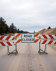 Road closed barrier on a dirt road with trees and sand piles in the background