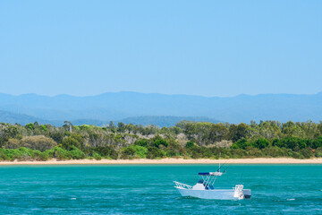 Australian coast, seaside landscape with blue water, sandy shore and mountains in the background, anchored boat at sea, summer sunny day.