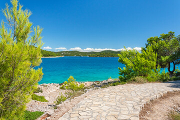 A natural rocky coastline with clear blue waters. A view from the coastal path to distant green islands on a sunny day.