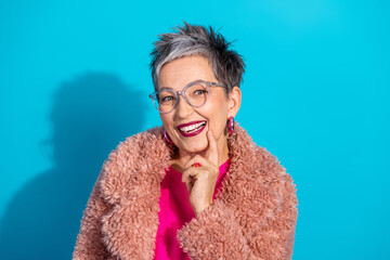 Glamorous mature woman with short grey hair wearing a pink coat smiles in a studio portrait against...