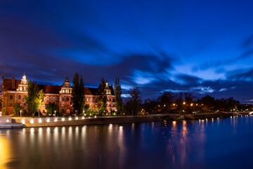 Fototapeta premium Night Riverside Cityscape With Historic Building And Water Reflections. Long Exposure Blue Hour Cityscape.