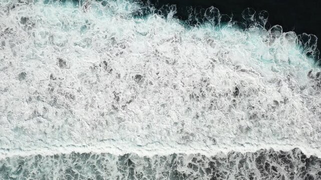 Aerial view of the ocean's furious white waves crashing against the dark shoreline, creating a dynamic contrast of textures and tones, Benijo, Santa Cruz de Tenerife, Spain.