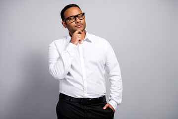 Thoughtful young handsome business professional in a white shirt and black pants stands against a grey background contemplating ideas for work
