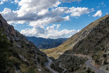 Naklejka premium Scenic winding road through a rugged mountain valley under a dramatic sky