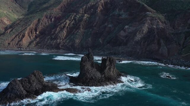 Aerial view of the dramatic Roque de las Animas rock formations piercing the turquoise ocean near the rugged coastline, Santa Cruz de Tenerife, Spain.