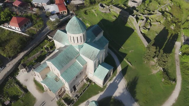 Aerial view of the ancient Bagrati Cathedral with its weathered stone and verdant dome, nestled amidst green lawns and historic ruins, Kutaisi, Imereti, Georgia.
