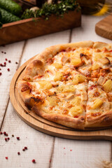 Classic Hawaiian pizza topped with pineapple, cheese and ham served on a wooden board on rustic table
