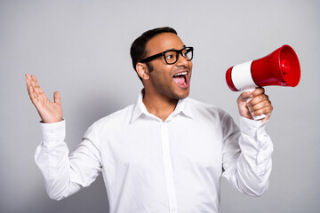 Young handsome businessman with megaphone presenting in office wearing white shirt and glasses