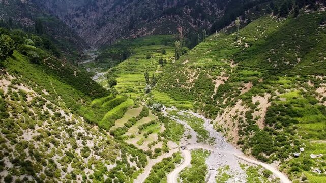 Aerial drone of Kunar Province, a seasonal stream winds through lush valleys, a tranquil oasis in Afghanistan's rugged terrain, inviting all to immerse in its beauty.