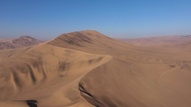 Wind shaped S curve dunes rise and fall in smooth patterns across a quiet Peruvian desert expanse