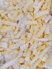 Full-Frame Background of Frozen, Uncooked Crinkle-Cut French Fries or Potato Sticks on Ice