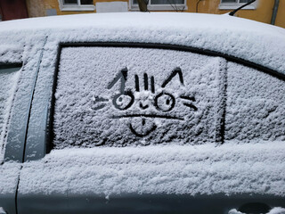 A funny cat is drawn on the side window of a car in the fresh snow
