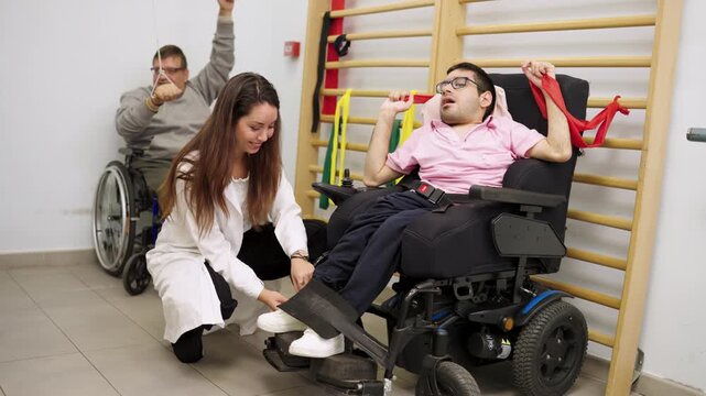 Men with disabilities in wheelchairs doing rehabilitation exercises with elastic bands. A female physiotherapist is helping a young man adjust his position