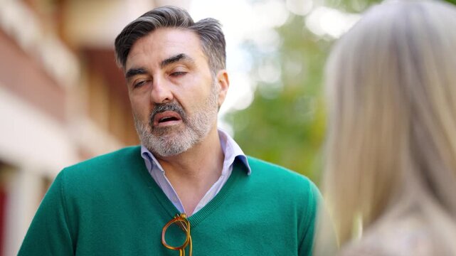 Middle aged man with a gray beard seriously talking and listening to a woman. He gestured and then his expression changes to serious