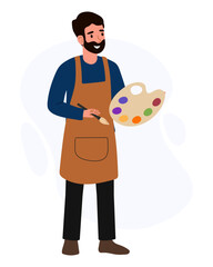 Man holds a paint palette while wearing an apron and smiling in an art studio during daytime