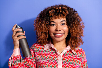 Young chic female smiles as she holds a spray can against a blue background wearing a bold zigzag blouse