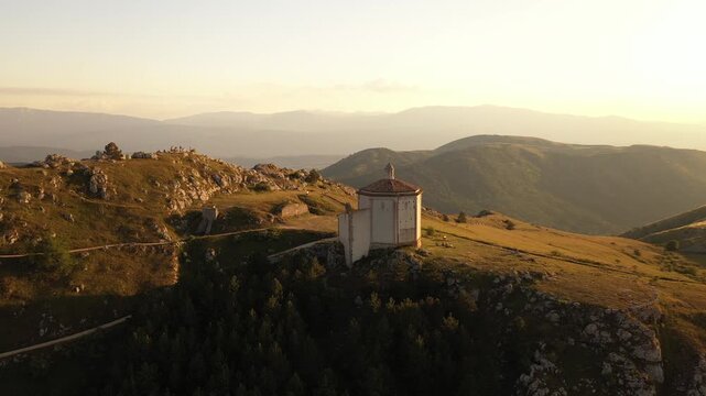 Aerial view of the octagonal Santa Maria della Pieta perched atop a hill, surrounded by rugged terrain bathed in the warm glow of the setting sun, Calascio, Abruzzo, Italy.
