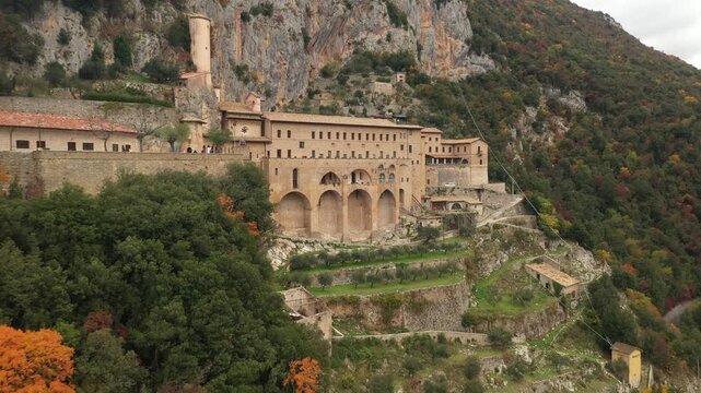 Aerial view of the historic Monastery of St. Benedict clinging to the rocky hillside surrounded by lush greenery, Subiaco, Lazio, Italy.