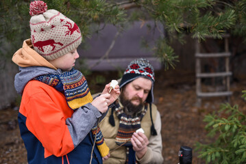 Father and son in winter clothes stringing marshmallows onto sticks for roasting outdoors