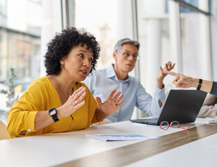 A group of businesspeople are gathered around a table, discussing something. Scene is serious and focused, as the group appears to be engaged in a discussion or decision-making process. There is a lot