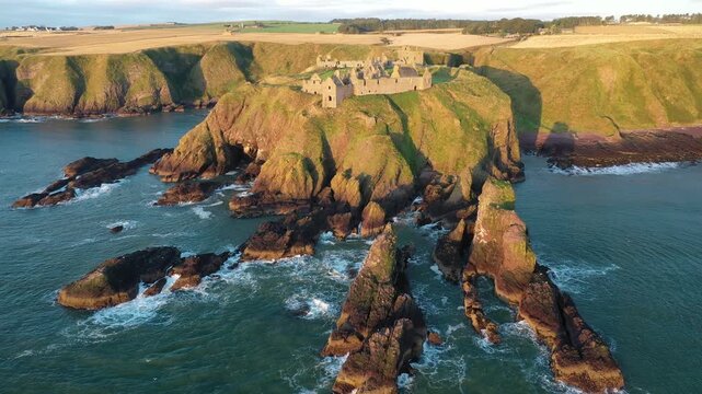 Aerial view of Dunnottar Castle on cliffs above the sea, with a dramatic interplay of light and shadow on the rocks, Stonehaven, Scotland, United Kingdom.
