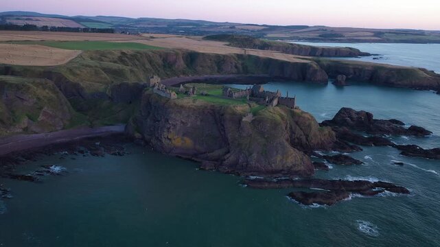 Aerial view of the historic Dunnottar Castle ruins perched atop a dramatic cliff, overlooking the dark blue ocean waters, Stonehaven, Scotland, United Kingdom.