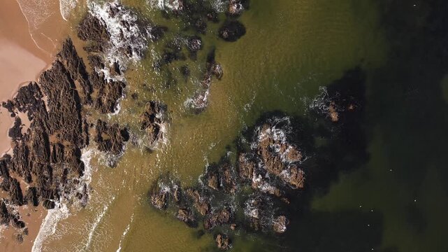 Aerial view of the rugged shoreline where the golden beach meets the rocky coast and the dark ocean waters, Stonehaven, Scotland, United Kingdom.