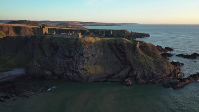 Aerial view of Dunnottar Castle ruins atop rugged cliffs meeting the serene sea, a blend of history and nature's grandeur, Stonehaven, Scotland, United Kingdom.