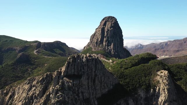 Aerial view of the majestic Roque de Agando, a volcanic plug rising dramatically amidst lush green hills, Vallehermoso, Canary Islands, Spain.