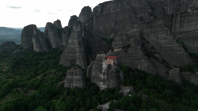 Aerial view of the Holy Monastery of Rousanou perched atop a towering rock formation amidst lush greenery, Meteora, Greece.